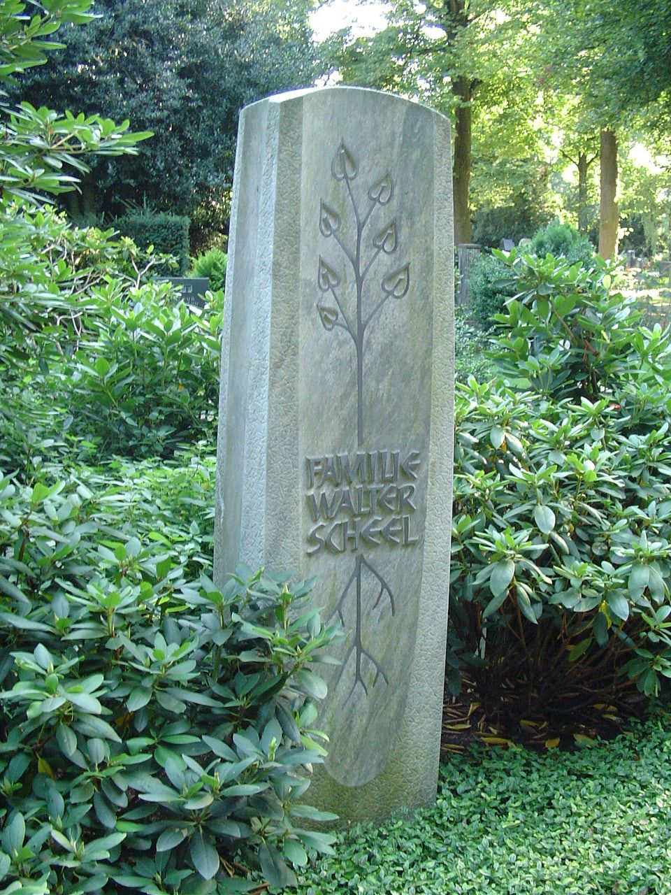 Schmale helle Stele der Familie Walter Scheel mit stilisiertem Baum zwischen Rhododendren auf Nordfriedhof Düsseldorf
